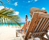 Eine Person hält im Liegestuhl am Strand ein Smartphone