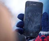 Eine Hand im Wollhandschuh hält ein iPhone, auf dem sich Eisblumen bilden