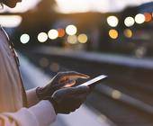 Frau mit Smartphone surft am BAhnsteig im Internet