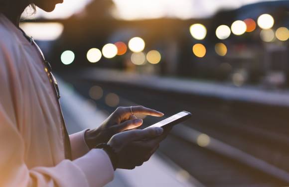 Frau mit Smartphone surft am BAhnsteig im Internet 