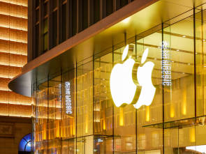 Symbolbild zeigt ein leuchtendes Apple-Logo an einer gläsernen Gebäudefassade 