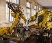 Zwei gelbe Industrieroboter-Arme bearbeiten zusammen ein Gerät