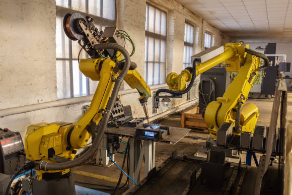 Zwei gelbe Industrieroboter-Arme bearbeiten zusammen ein Gerät 