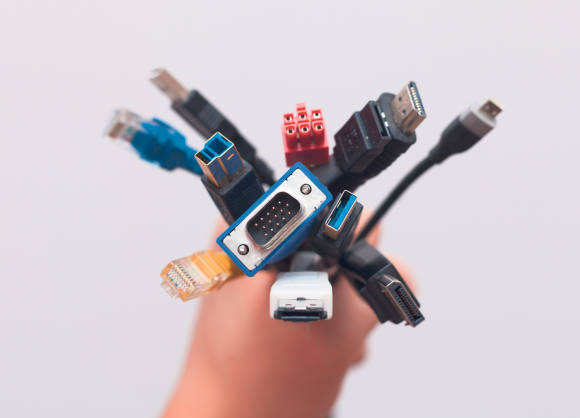 Eine Hand hält mehrere Kabel mit verschiedenen Steckern 