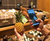 Frau scannt per Smartphone den Strichcode auf einer Ananas