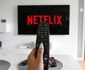 Eine Hand hält eine Fernbedienung, im Hintergrund ein TV mit Netflix-Logo