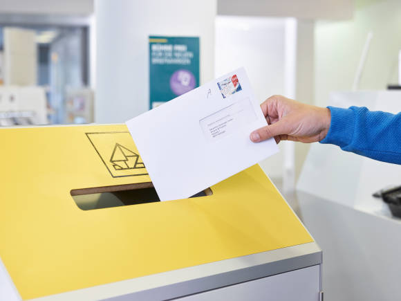 Eine Hand ist dabei, einen Brief in einen Briefkasten einzuwerfen 