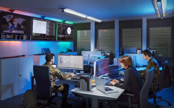 5 Personen, teils in Militärkleidung, arbeiten an ihren Computern 