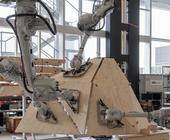Vier Roboterarme arbeiten an einer Holzkonstruktion