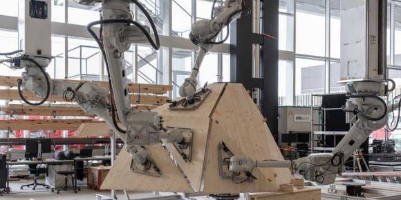 Vier Roboterarme arbeiten an einer Holzkonstruktion 