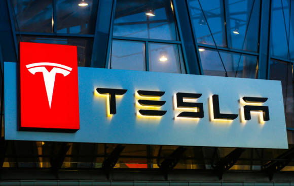 Beleuchtetes Tesla-Logo mit Schriftzug an einem Gebäude 