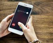 Hände halten ein Smartphone, auf dem das Display einen Anruf ankündigt