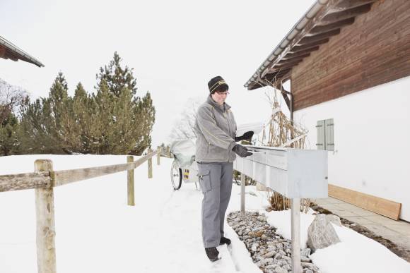 Eine Pöstlerin steckt Briefe in Briefkästen vor einem Haus 