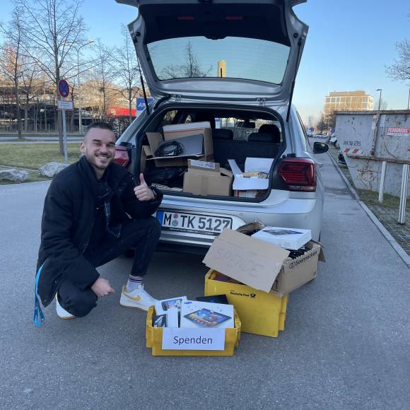 Ein junger Mann freut sich über Kartons voller Computer-Sachspenden 