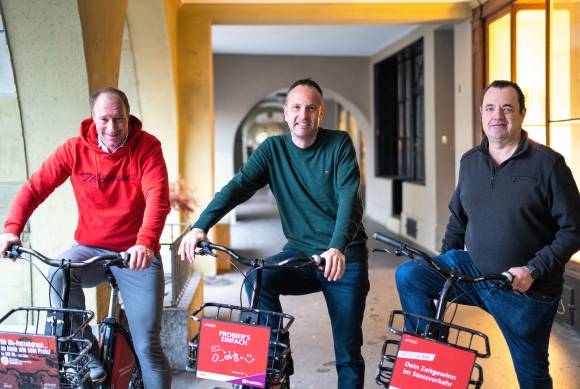 Die drei neuen Besitzer von Publibike sitzen auf einem E-Bike 