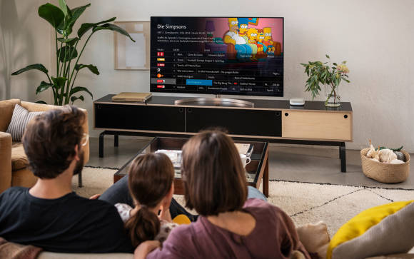 Eine Familie sitzt auf dem Sofa und inspiziert das TV-Programmangebot auf ihrem Smart-TV