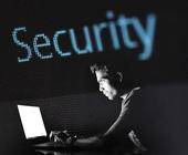 Mann am Laptop, Schriftzug Security, dunkler Hintergrund