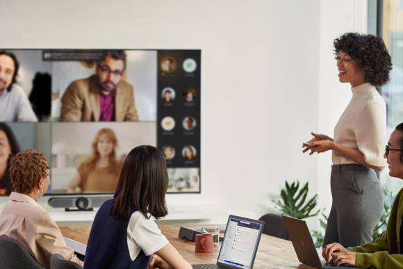 Hybrides Teams-Meeting: Einige Personen in Teams auf dem grossen TV, einige Personen sind im Sitzungszimmer persönlich anwesend 