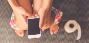 Person mit Smartphone auf Toilette 