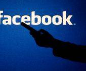 Facebook-Logo und Silhouette einer Hand mit Smartphone