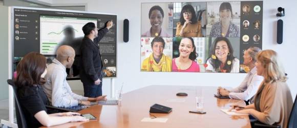 Symbolbild zeigt Konferenzraum mit Teams-Teilnehmenden auf der Leinwand 