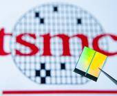 TSMC-Logo im Hintergrund, im Vordergrund hält eine Pinzette einen Chip