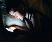 Ein Kind liegt im Bett und hält ein Smartphone