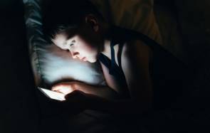 Ein Kind liegt im Bett und hält ein Smartphone 