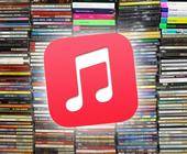 Im Vordergrund steht das Symbol der Musik-App von Apple; im unscharfen Hintergrund sind einige Stapel mit CDs zu sehen