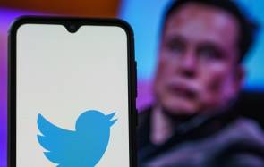 Twitter-Logo auf einem Smartphone, daneben im Hintergrund Elon Musk 