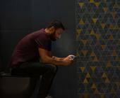 Ein Mann sitzt auf dem Klo und schaut auf sein Smartphone