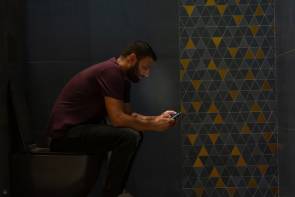 Ein Mann sitzt auf dem Klo und schaut auf sein Smartphone 