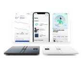 Die Personenwaage im Vordergrund (schwarz, weiss), im Hintergrund die zugehörigen Apps auf einem Smartphone