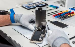 Aus einem geöffneten Smartphone-Gehäuse entnimmt jemand mit Antistatikhandschuhen und Pinzette ein kleines Bauteil 