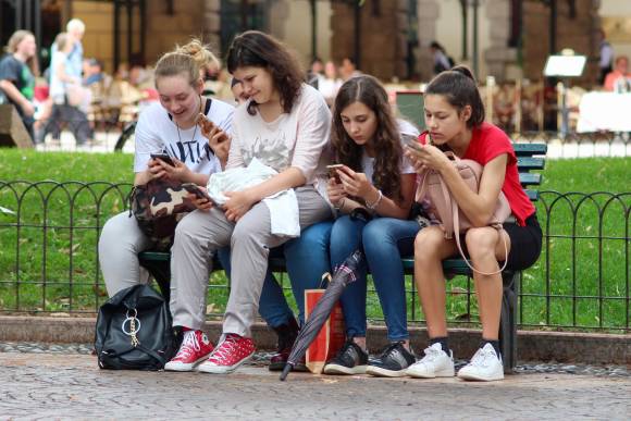 Vier Mädchen sitzen nebeneinander auf einen Bank und schauen auf ihre Smartphones 