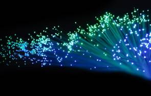 Symbolbild zeigt viele grün und blau leuchtende Glasfasern vor schwarzem Hintergrund 