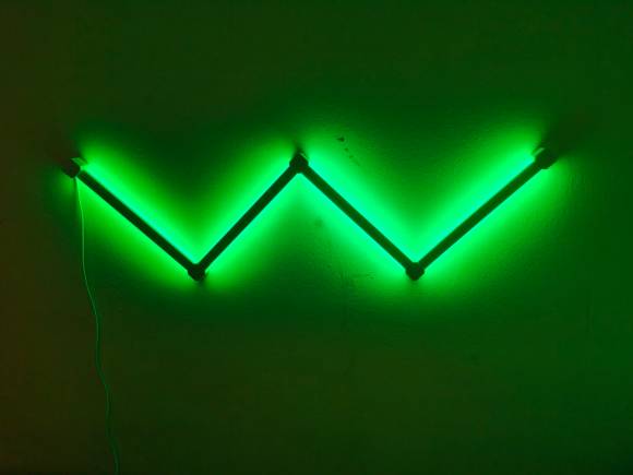 Grün leuchtende Nanoleaf-Elemente an einer Wand formen ein W 