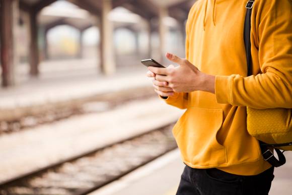 Symbolbild zeigt einen Mann am Bahngleis mit Smartphone in der Hand 