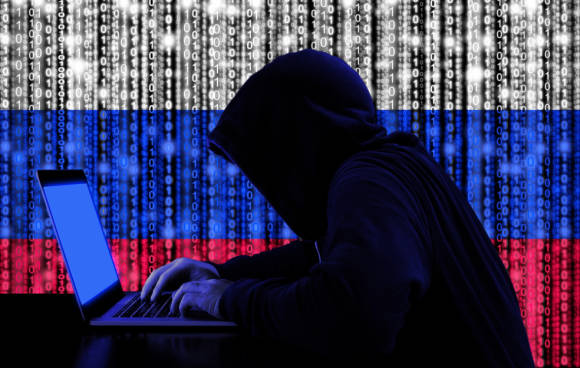 Symbolbild eines Hackers mit Hoodie vor einer russischen Flagge 