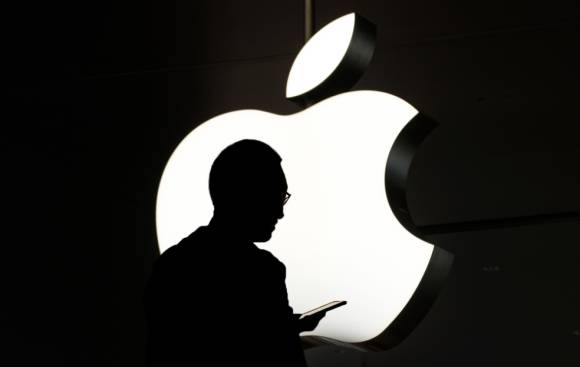 Silhouette einer Person mit Smartphone vor einem weissen Apple-Logo 