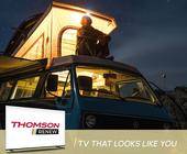 Thomson-TV-Banner zeigt Mann, der nachts auf dem Dach seines Campers sitzt