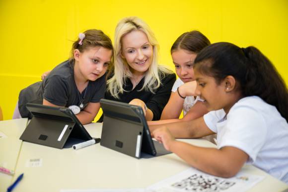 Drei Mädchen und eine Frau sitzen an einem Tisch mit zwei Notebooks 