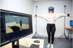 Eine Frau mit VR-Brille imitiert die Bewegung eines Avatars, das auf einem Bildschirm zu sehen ist 